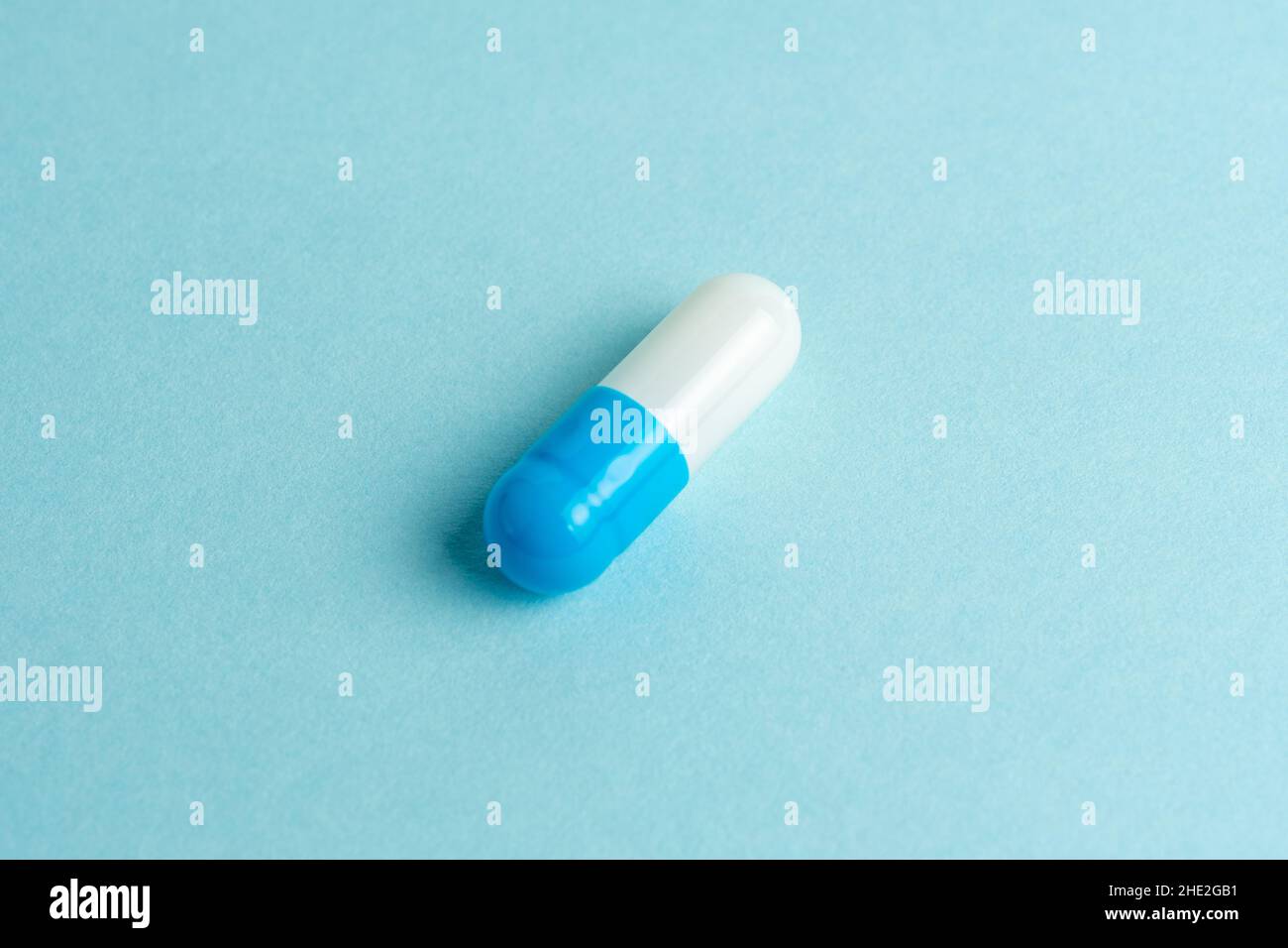 Capsula di pillola bianca-blu su sfondo blu. Concetto di farmacia minimo. Disposizione piatta. Foto Stock