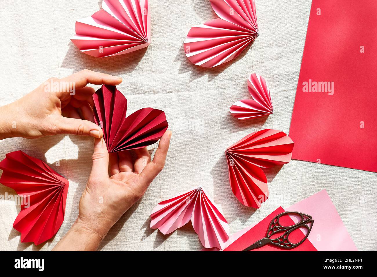 Le mani della donna che fanno i cuori della carta. Ghirlanda Origami.  Simbolo d'amore per il giorno di San Valentino, buon compleanno, saluti,  giorno delle madri, giorno delle donne. Fai da te.