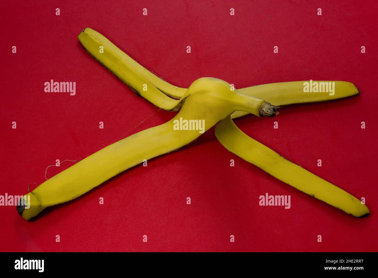 Pelle di banana gialla su sfondo rosso. Concetto di avvertenza su superfici scivolose e pericolo di scivolamento. Primo piano Foto Stock