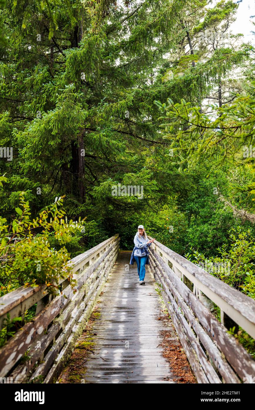 Donna anziana escursioni attraverso ponte di legno; Tahkenitch Creek Trail; vicino a Reedsport; Oregon; Stati Uniti Foto Stock