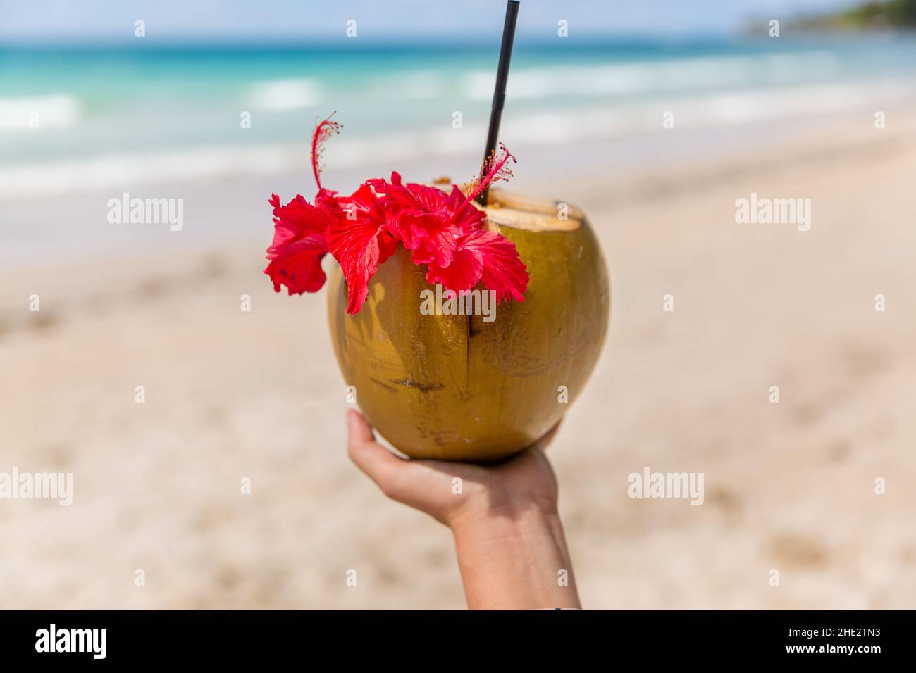 Cocktail al cocco in mano di una donna su una spiaggia di sabbia bianca Foto Stock