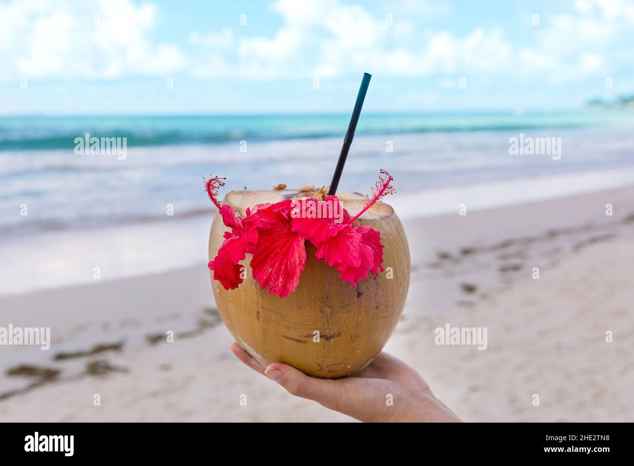 Cocktail al cocco in mano di una donna su una spiaggia di sabbia bianca Foto Stock