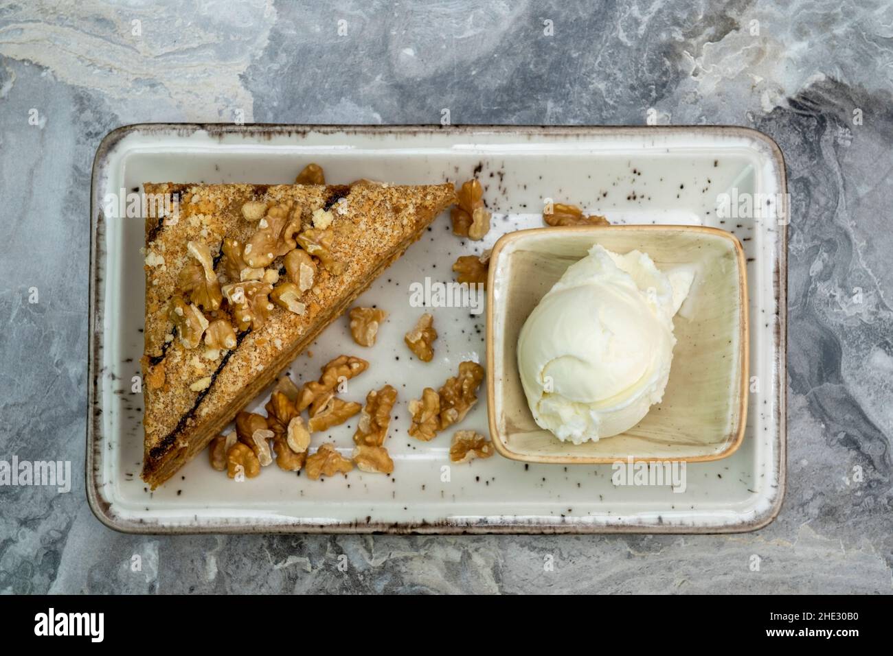 Una fetta di torta di noci e gelato in un piatto di porcellana su un pavimento di marmo Foto Stock