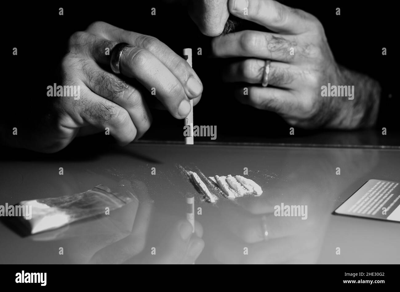 Quest'uomo sta russando la polvere di cocaina con la banconota laminata. Concetto di narcotici. Versione in bianco e nero. Foto Stock