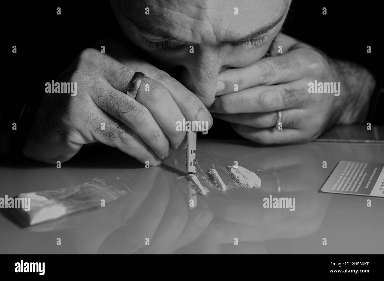 Quest'uomo sta russando la polvere di cocaina con la banconota laminata. Concetto di narcotici. Versione in bianco e nero. Foto Stock