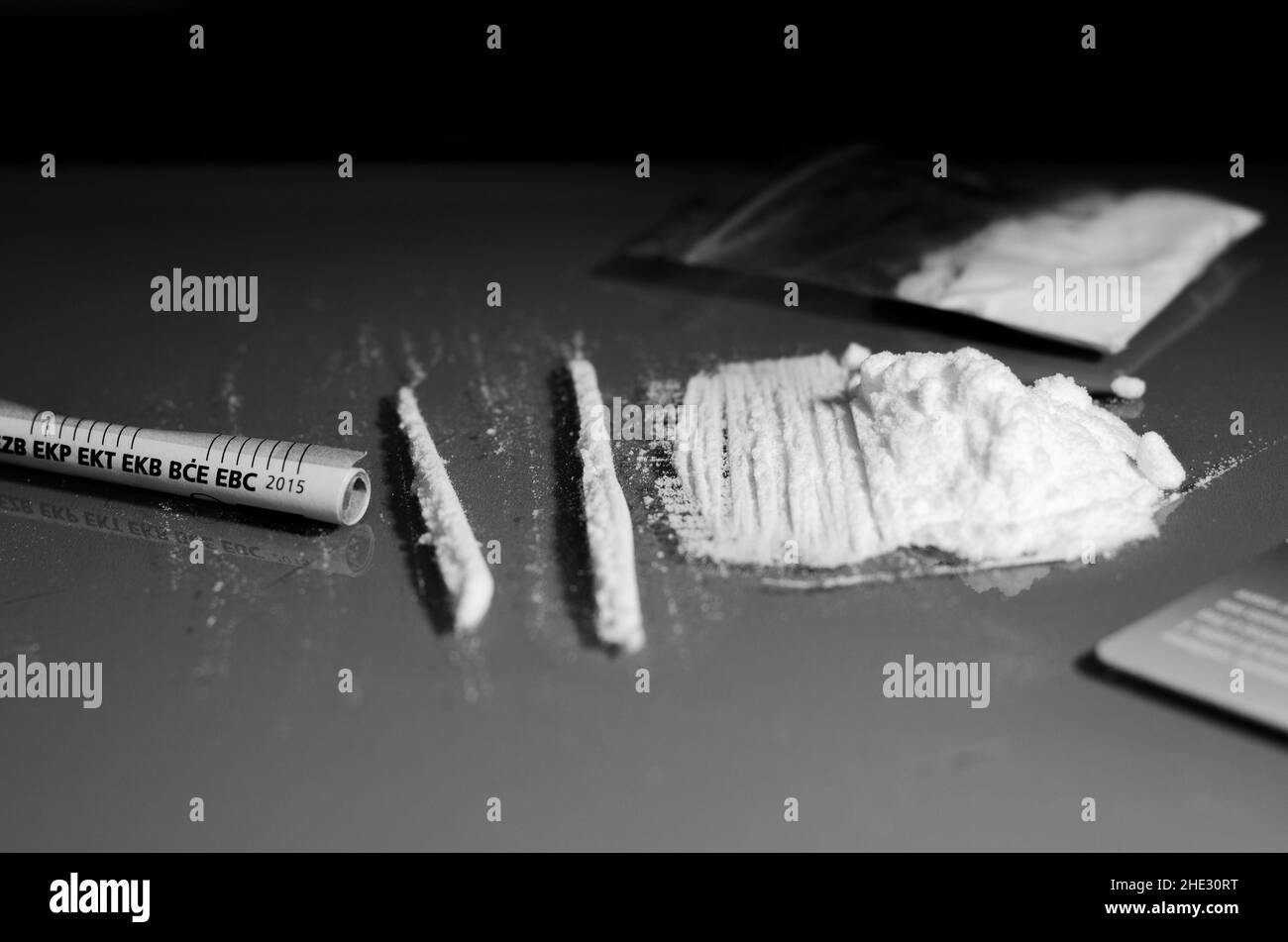 Busta, pila e banconota rotolata. Cocaina divisa in strisce su uno sfondo a specchio chiaro. Primo piano. Concetto di narcotici. Versione in bianco e nero. Foto Stock