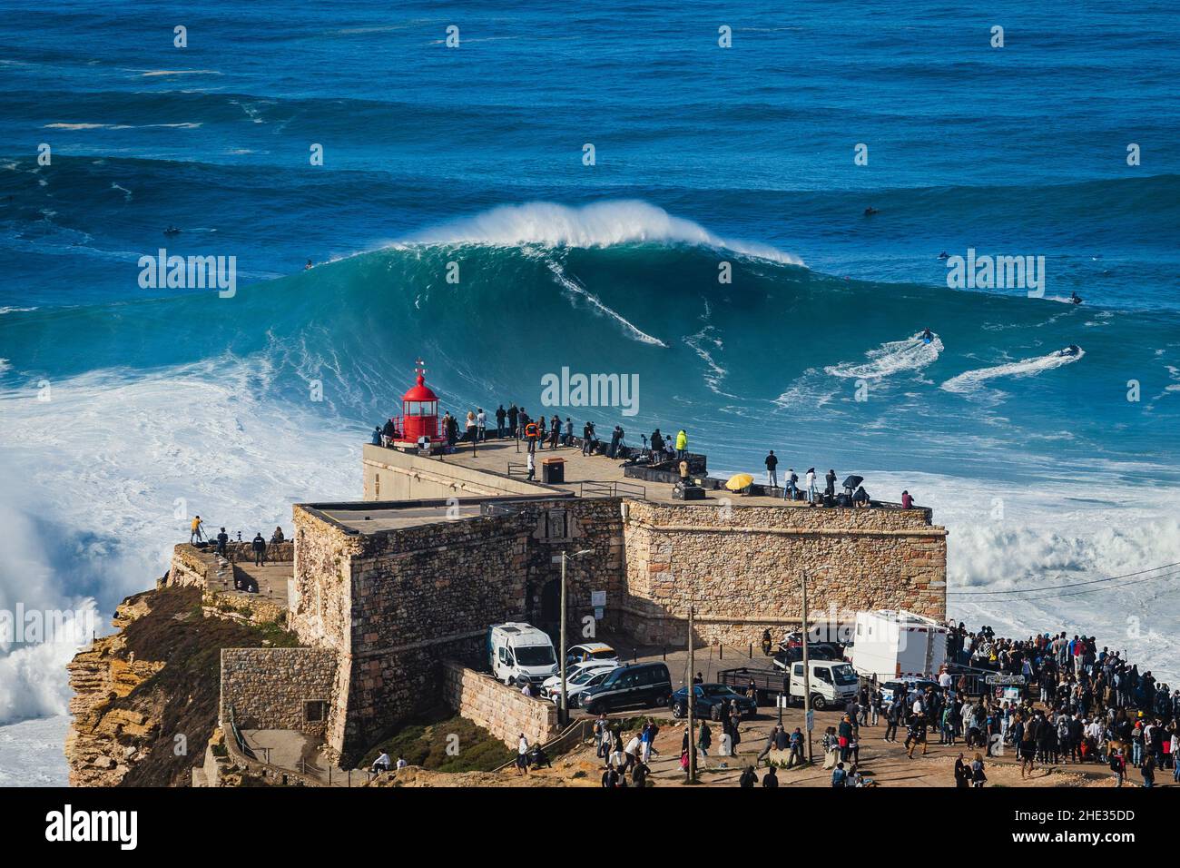 Surfista che cavalca un'onda enorme vicino al faro di Sao Miguel Arcanjo a Nazare, Portogallo. Nazare è noto per avere le onde più grandi in t Foto Stock