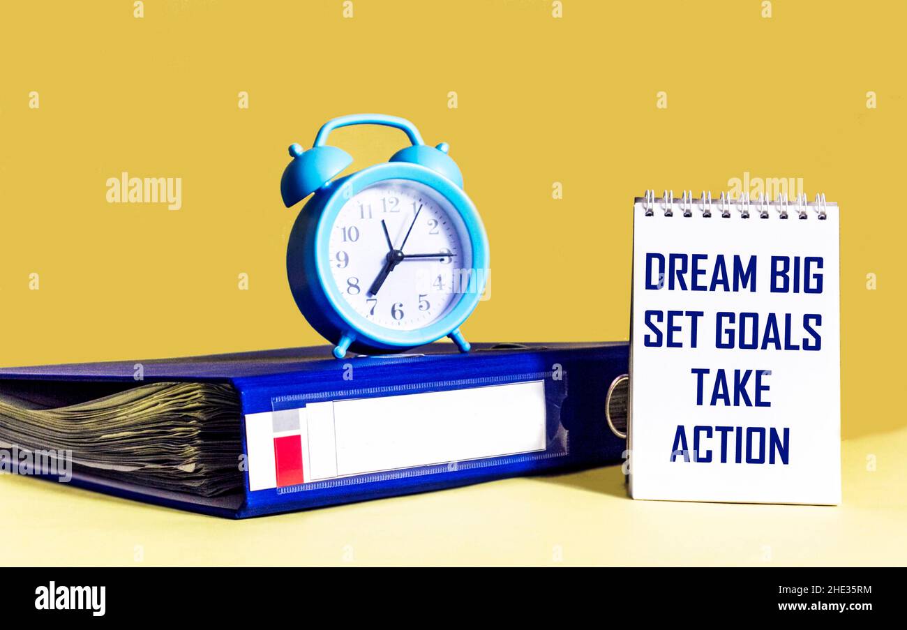 Dream Big - Imposta obiettivi - prendere azione, scrittura a mano in notebook con cartella e orologio su sfondo giallo Foto Stock