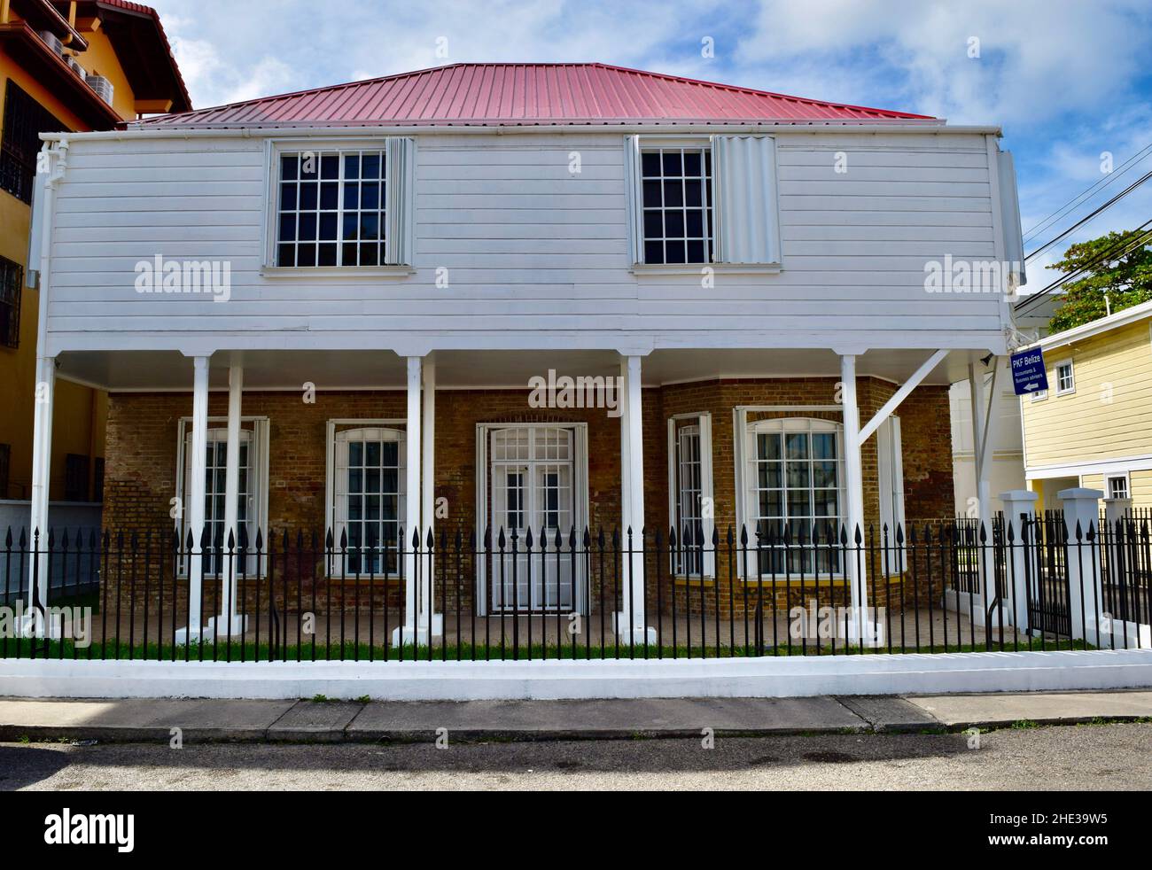 Un edificio restaurato con un tetto rosso, persiane uragano, e bar sulle finestre a Belize City, Belize Foto Stock