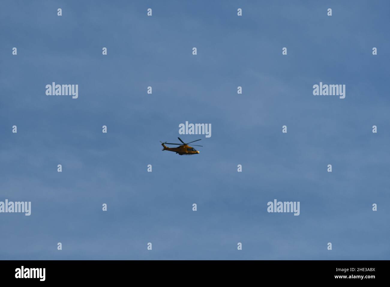 Un elicottero che vola in mezzo al cielo blu con le nuvole irregolari Foto Stock