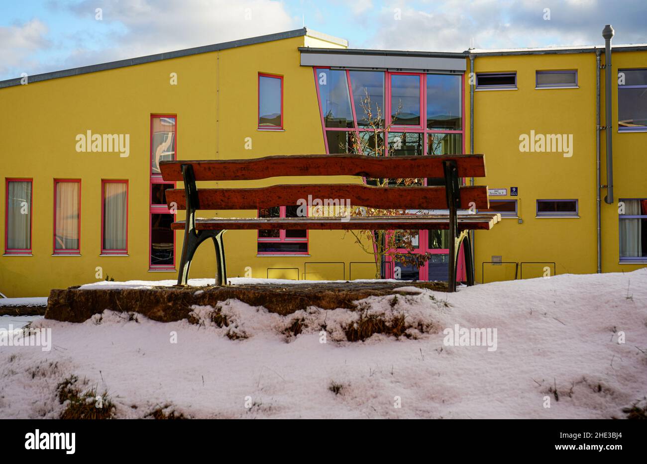 Una panchina su una piccola collina coperta di neve. Dietro un edificio scolastico al Campus Rudolf Steiner Waldorf School di Monaco in inverno. Foto Stock