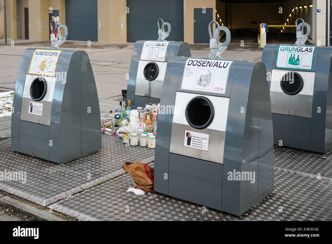 Quattro moderni contenitori in alluminio per materiali riciclabili di fronte all'ingresso di un parcheggio sotterraneo. Le bottiglie sono poste vicino ai contenitori. Foto Stock