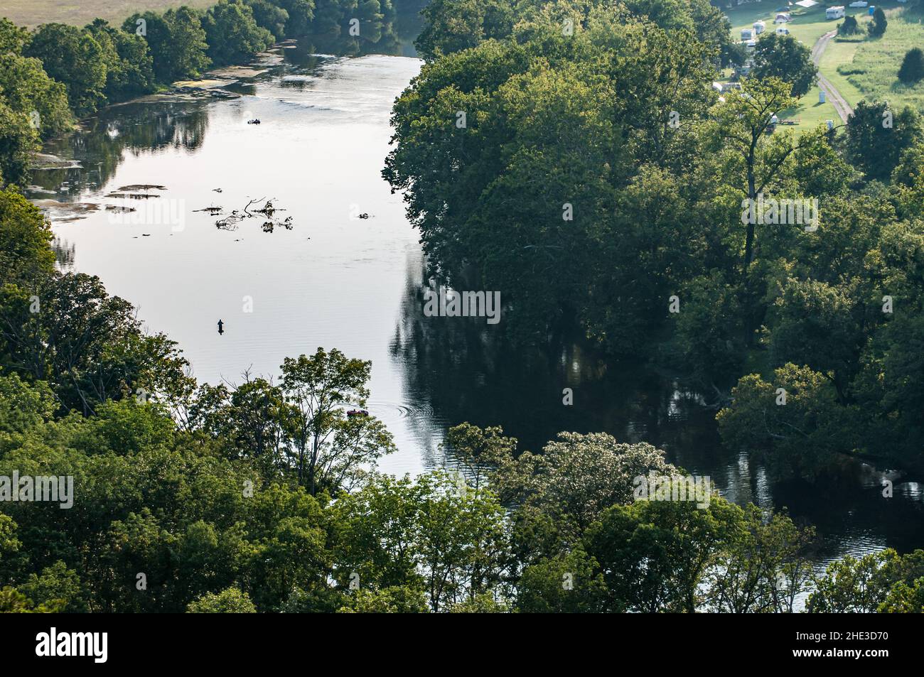 Un pescatore vade nel fiume Shenandoah mentre i burfters vengono intorno ad un'ansa del fiume. Mostra banche boschive con case dietro su un terreno più alto. Foto Stock