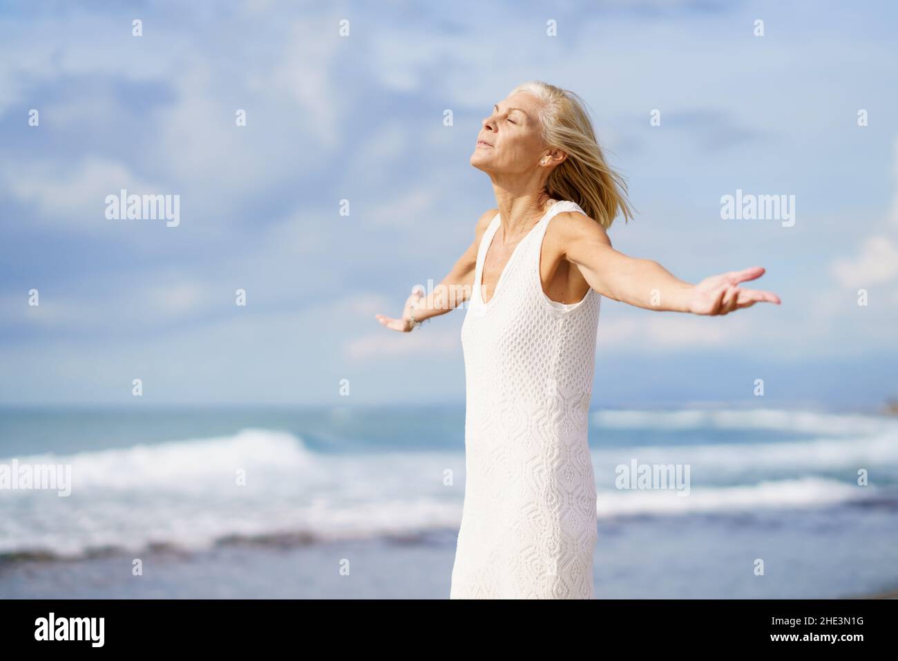 Donna matura respirando l'aria della spiaggia con gli occhi chiusi e le braccia aperte. Foto Stock