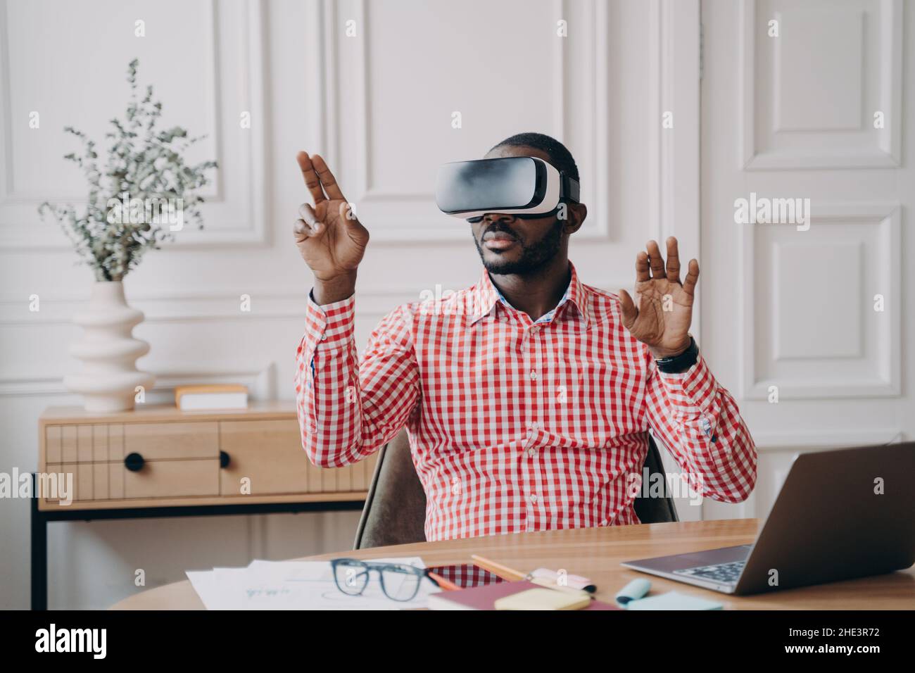 Un uomo d'affari afro-americano concentrato che utilizza il visore VR, sperimentando la realtà virtuale giocando al gioco Foto Stock