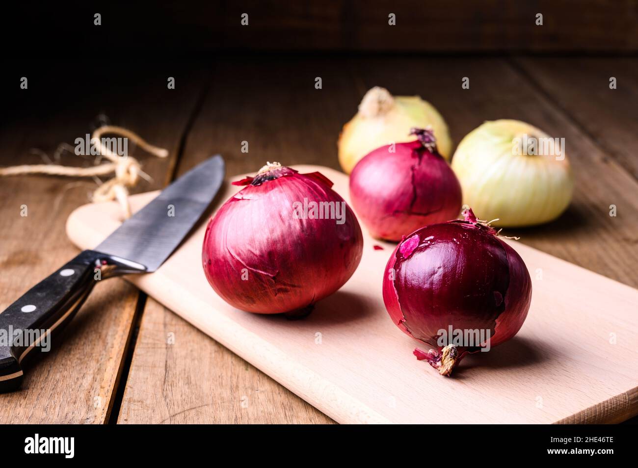 Cipolle rosse e bianche su un tagliere di legno e coltello su un rustico tavolo di legno in cucina, vista dall'alto. Foto di alta qualità Foto Stock