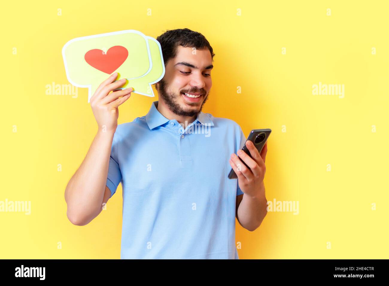 Il giovane uomo tiene un fumetto con un cuore e ha usato lo smartphone. Concetto di social media. Foto Stock