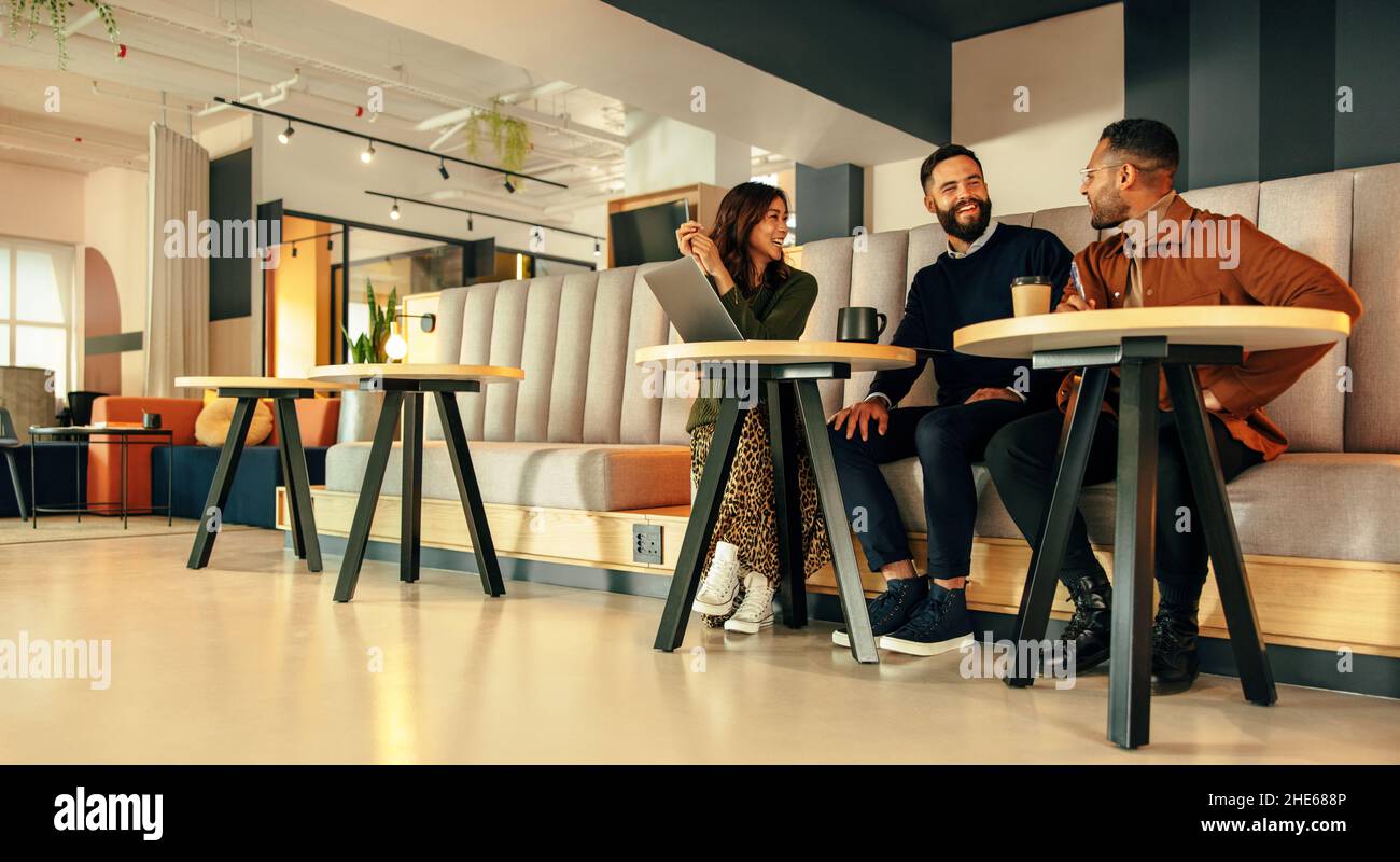 Tre uomini d'affari che lavorano in una lobby d'ufficio. Team di uomini d'affari felici sorridendo mentre si ha una discussione. Gruppo di imprenditori moderni coll Foto Stock