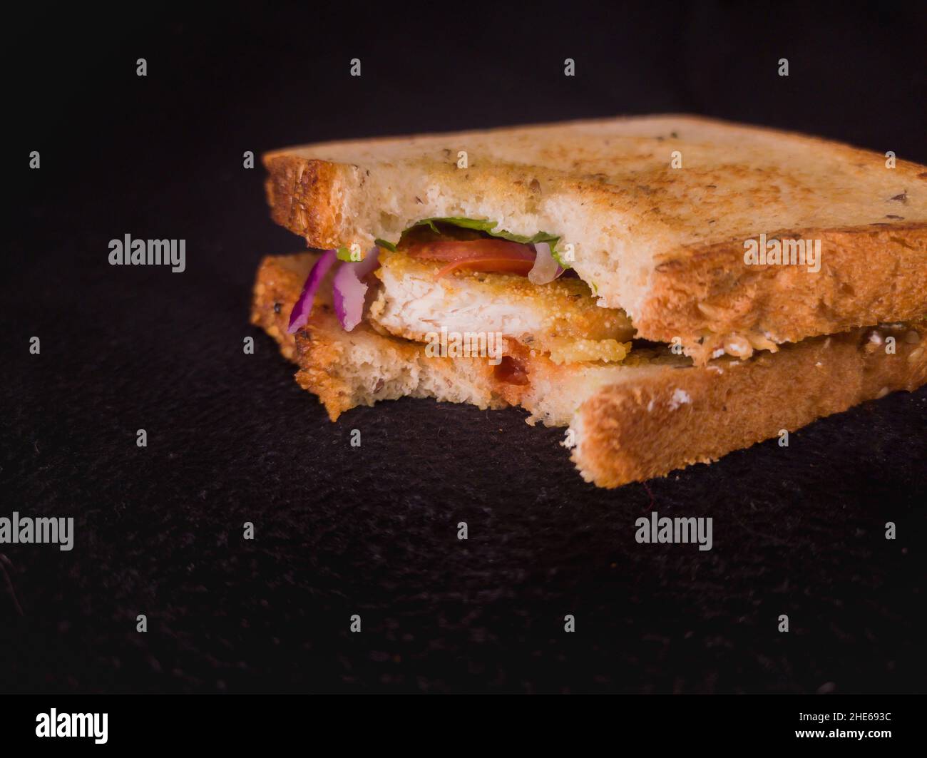 sandwich grigliato con pomodoro, cipolla, pollo, lattuga e pane multigrain. primo piano con spazio copia e sfondo scuro. Foto Stock
