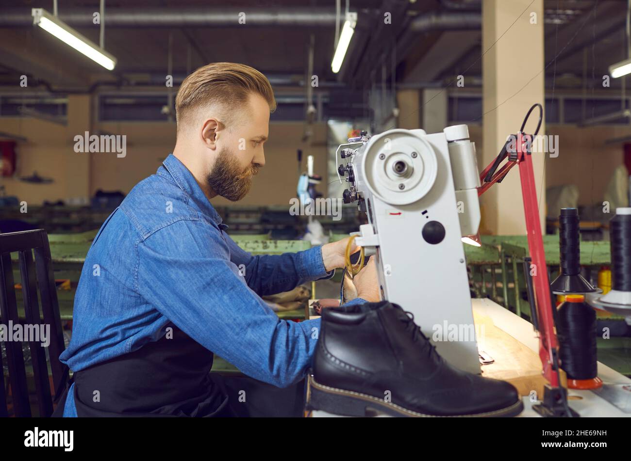 Operatore di fabbrica di scarpe che utilizza una macchina da cucire industriale per realizzare nuovi stivali in pelle nera Foto Stock
