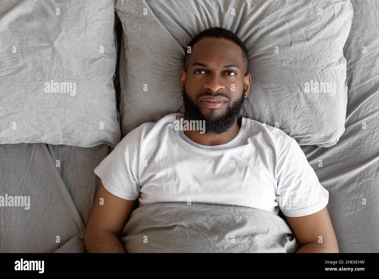 Uomo nero sdraiato a letto e pensiero, vista dall'alto Foto Stock