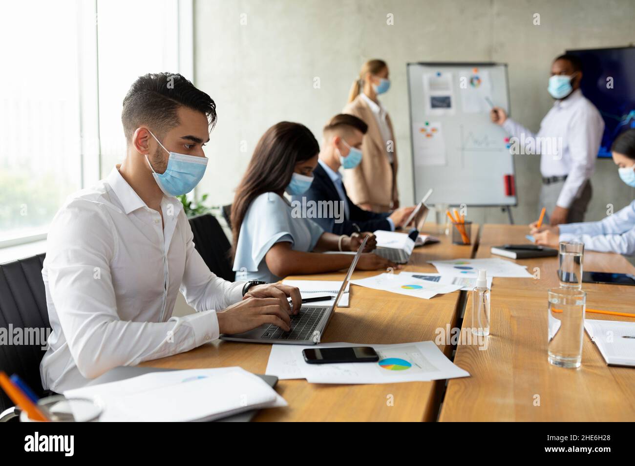 Gruppo di colleghi multietnici che indossano maschere mediche che hanno un incontro d'affari in ufficio Foto Stock