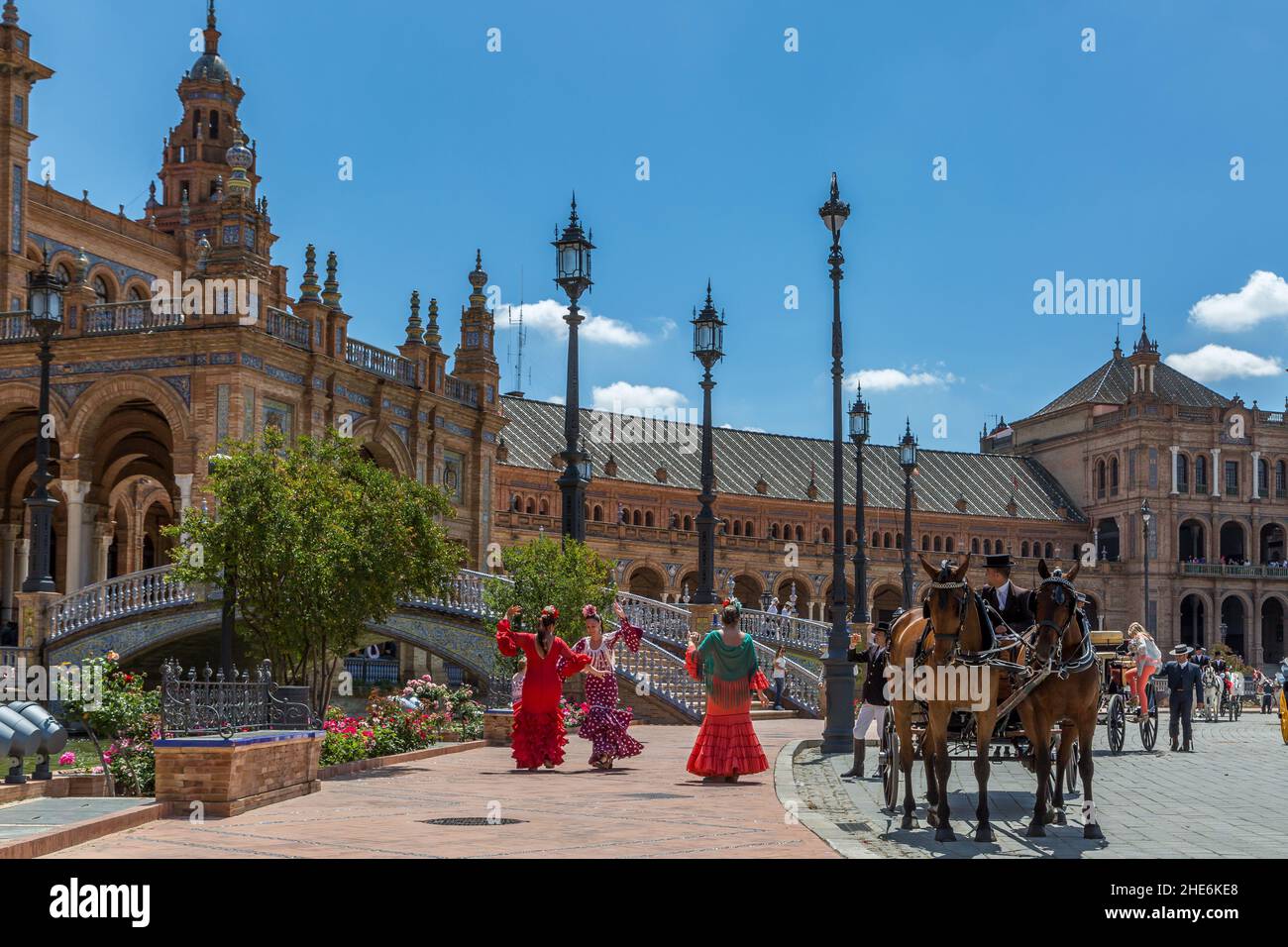 Le Signore in tradizionali costumi di flamenco ballano alla Plaza de Espana, mentre la loro carrozza trainata da cavalli attende per portarle alla Feria de Abril annuale. Foto Stock