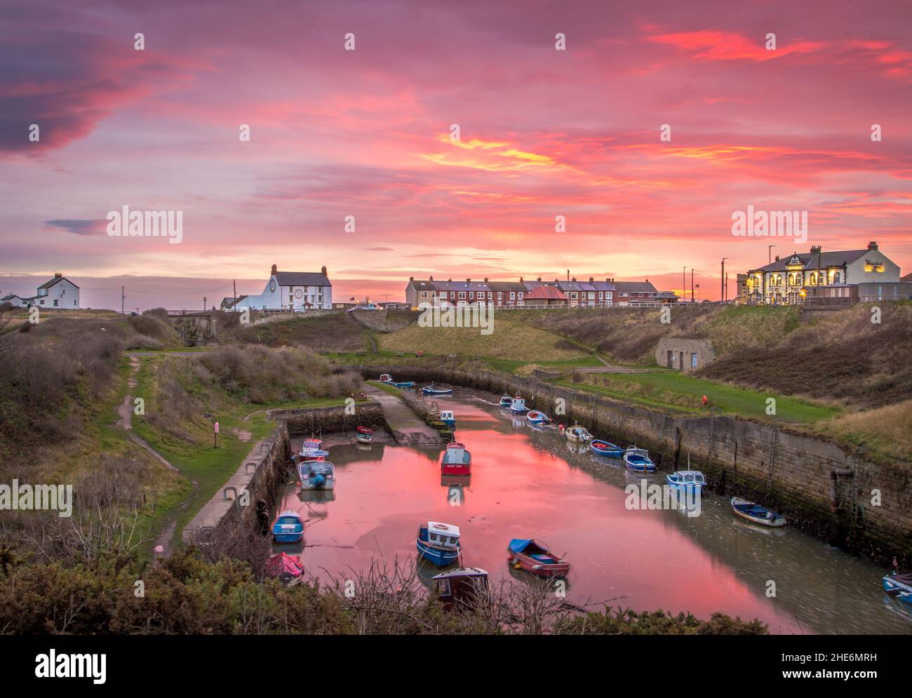 Il Burn con le barche da pesca ormeggiate di Seaton Sluice, Northumberland all'alba, con il cielo ardente che si riflette nell'acqua Foto Stock