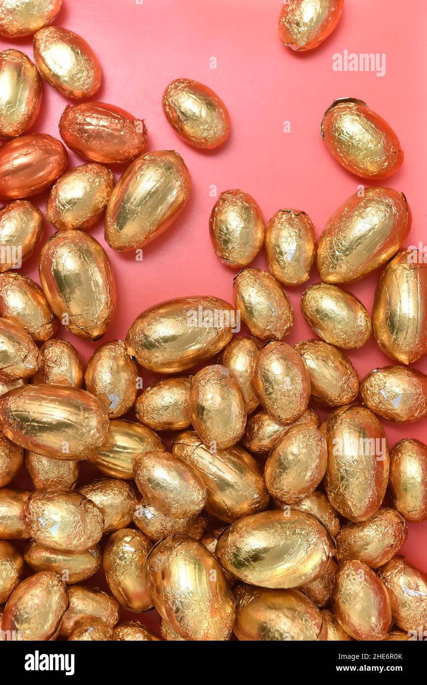 Mucchio grande e piccolo o gruppo di uova di pasqua di cioccolato avvolte con lamina d'oro, d'arancio e di bronzo, su sfondo arancione di pesca. Foto Stock