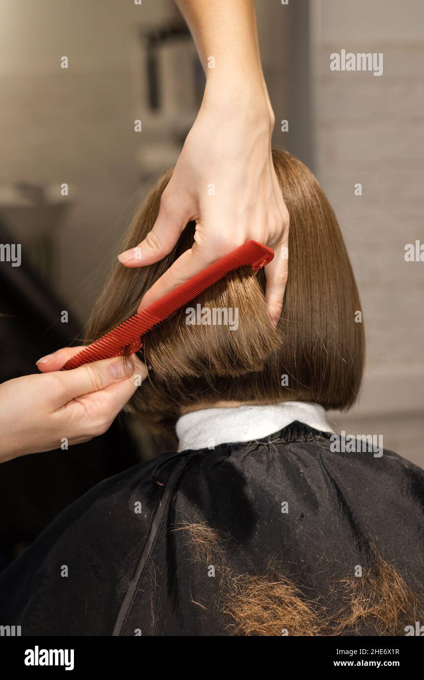 Closeup vista posteriore di ragazza di età preseena seduta in sedia in parrucchiere. Parrucchiere controllo del suo nuovo taglio di capelli Foto Stock
