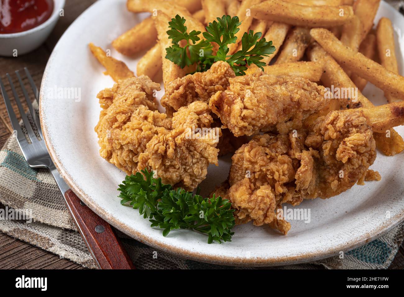 Croccanti polli fritti e patatine fritte guarnite con prezzemolo su un piatto Foto Stock