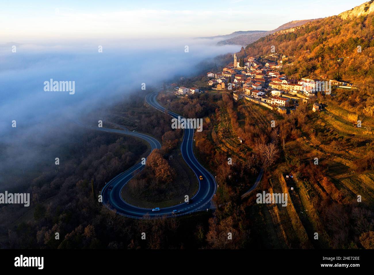 Vista aerea di una strada tortuosa parzialmente coperta di nebbia al tramonto, Kraski rob, villaggio di Crni Kal in Slovenia Foto Stock