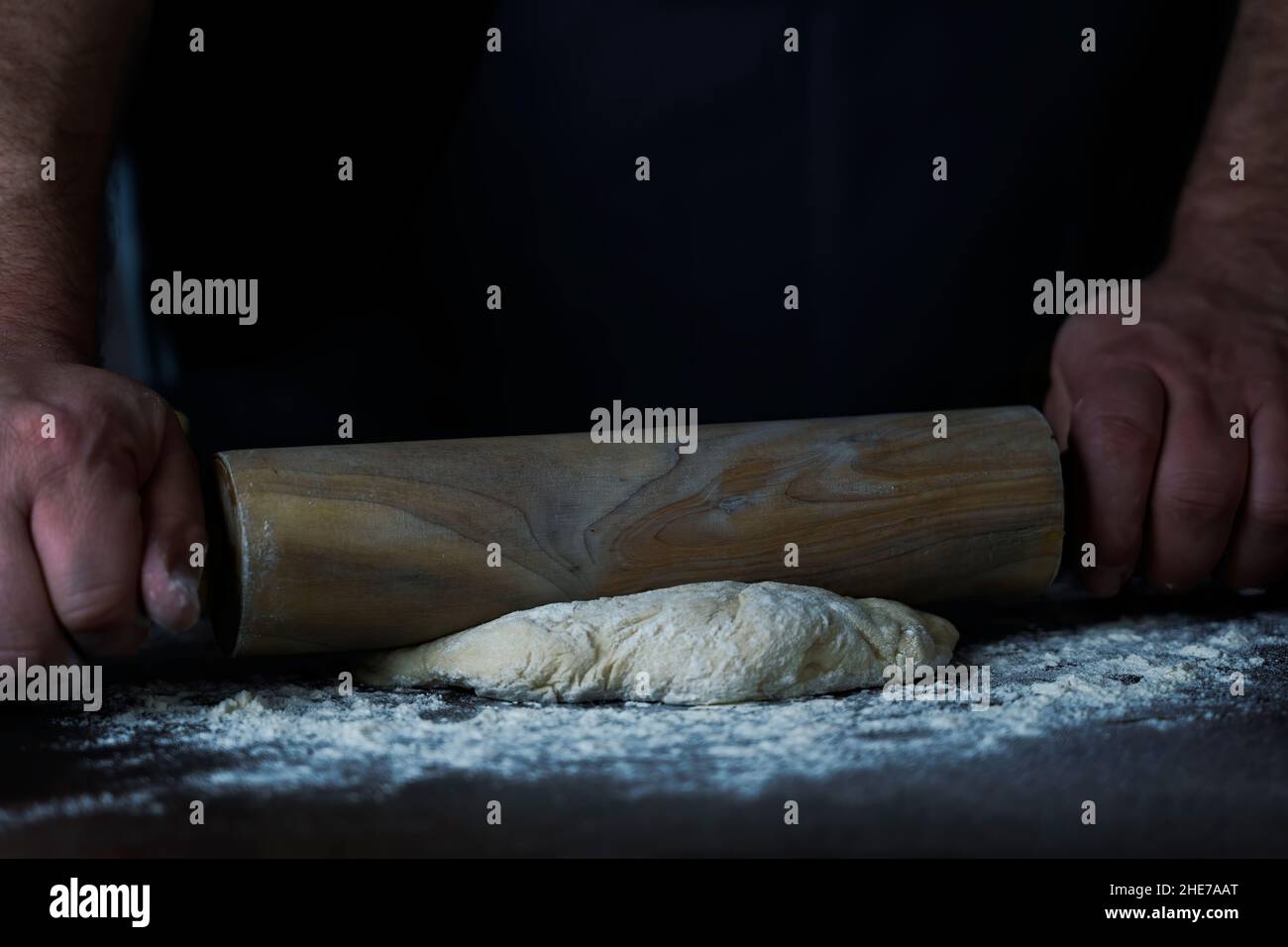 Man Baker o chef sta arrotolando l'impasto fresco con un rullo su una superficie di legno. Foto Stock