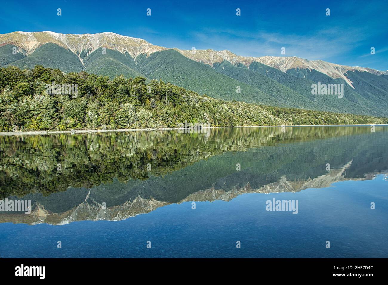 Vista panoramica del lago che riflette montagne coperte di foreste sotto il cielo nuvoloso Foto Stock