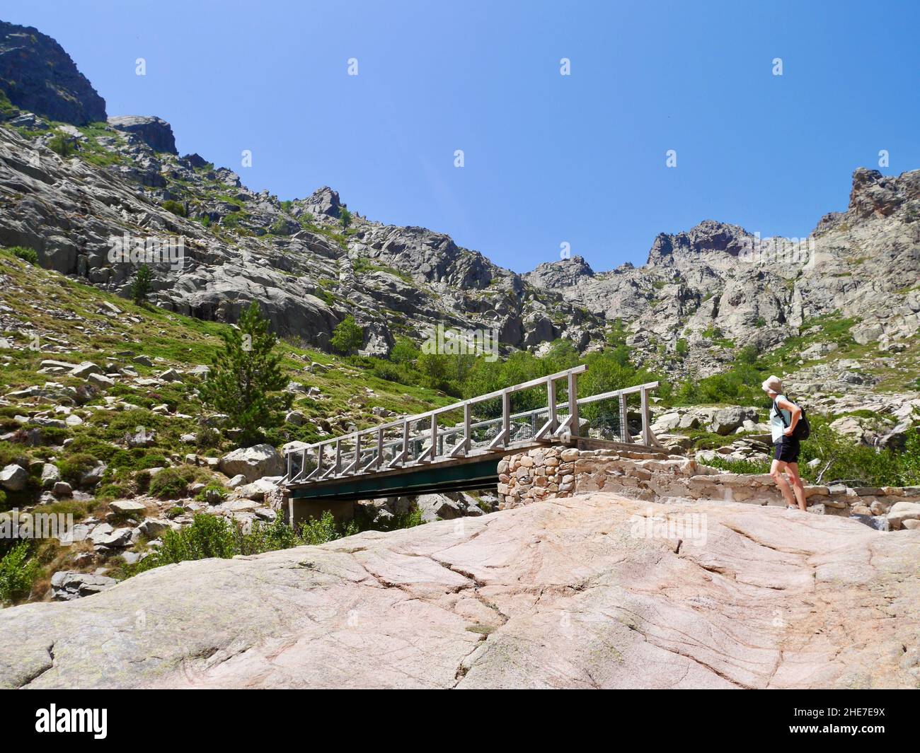 Escursionista che attraversa il ponte di legno sul Golf in montagne remote sulla strada per paglia Orba, Corsica, Francia. Foto Stock
