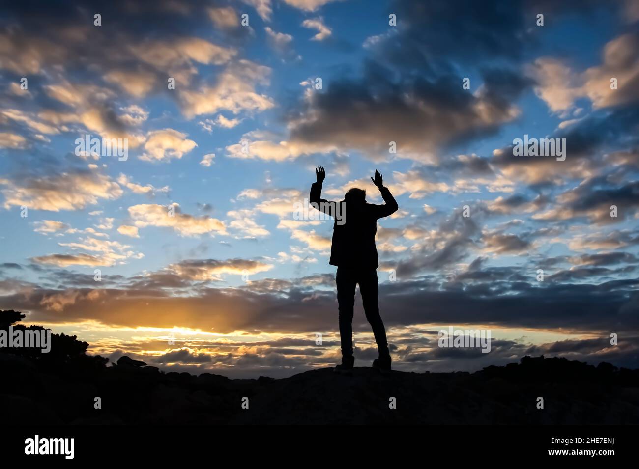 Silhouette di una persona sopra l'orizzonte contro il cielo blu nuvoloso Foto Stock