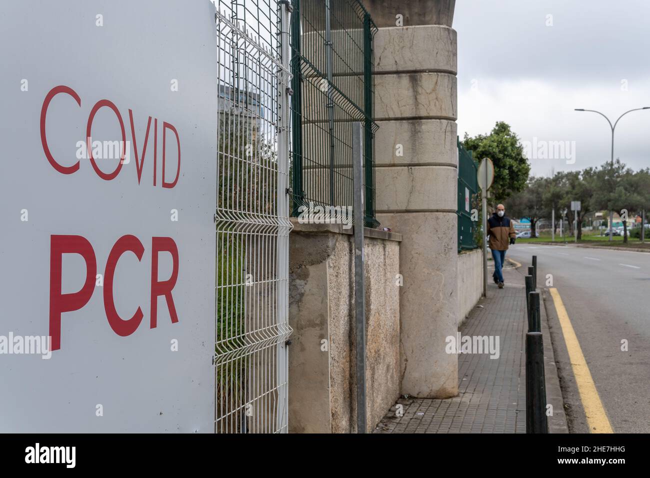 Primo piano di un poster della PCR Covid all'esterno di un centro di vaccinazione. Sullo sfondo, fuori fuoco, un uomo che indossa una maschera facciale Foto Stock