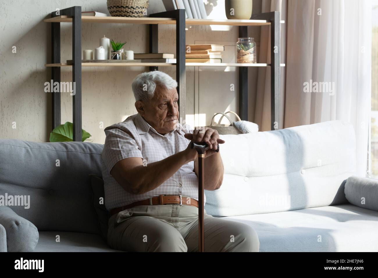 Uomo anziano stanco infelice con bastone poggiante sul divano. Foto Stock