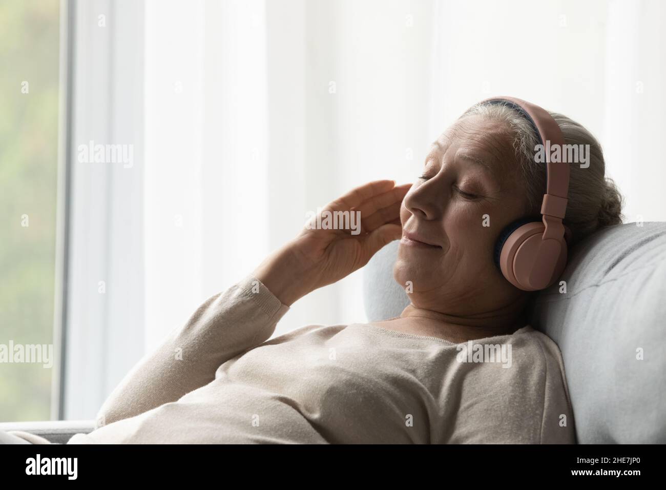 Donna dall'età media rilassata che ascolta musica in cuffia. Foto Stock