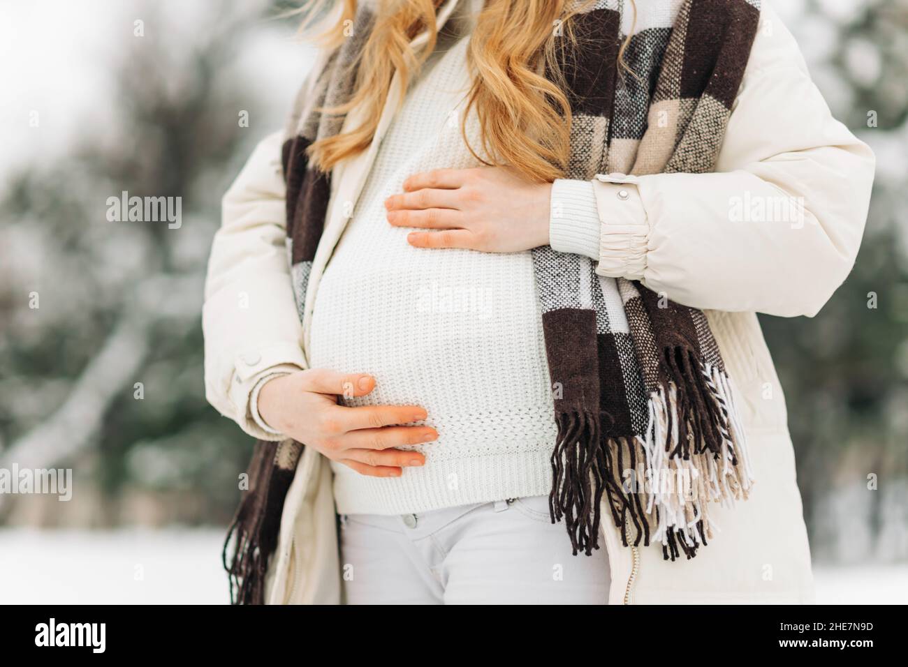 donna incinta in abiti invernali caldi in piedi all'esterno in una giornata  invernale nevosa, con le mani sul suo stomaco sullo sfondo della natura.  Concetto di pregna Foto stock - Alamy