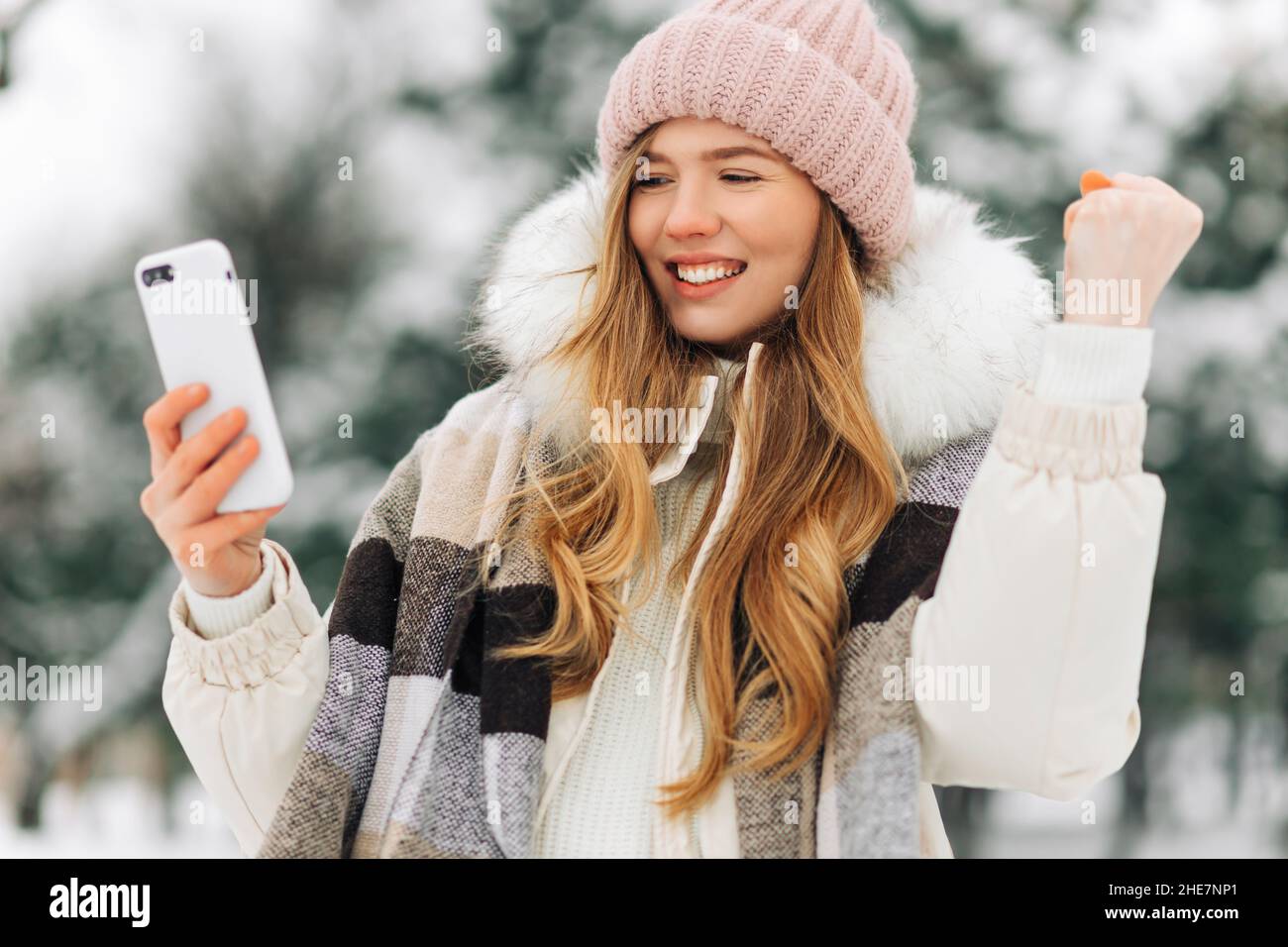 Ritratto di una donna entusiasta per strada nel tempo invernale, urlando e aggrappando il pugno, tenendo un cellulare nelle sue mani, gioendo Foto Stock
