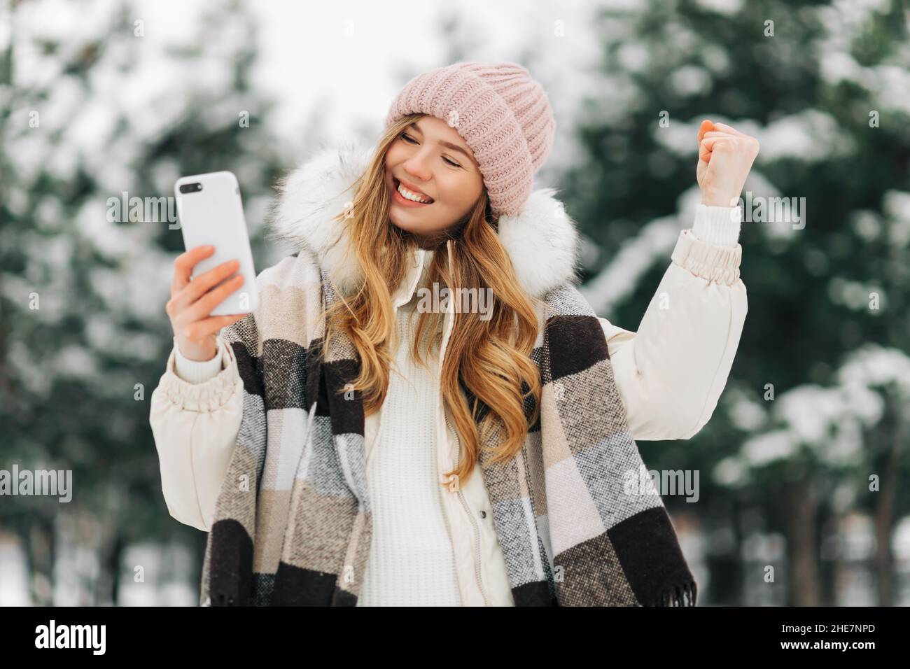 Ritratto di una donna entusiasta per strada nel tempo invernale, urlando e aggrappando il pugno, tenendo un cellulare nelle sue mani, gioendo Foto Stock