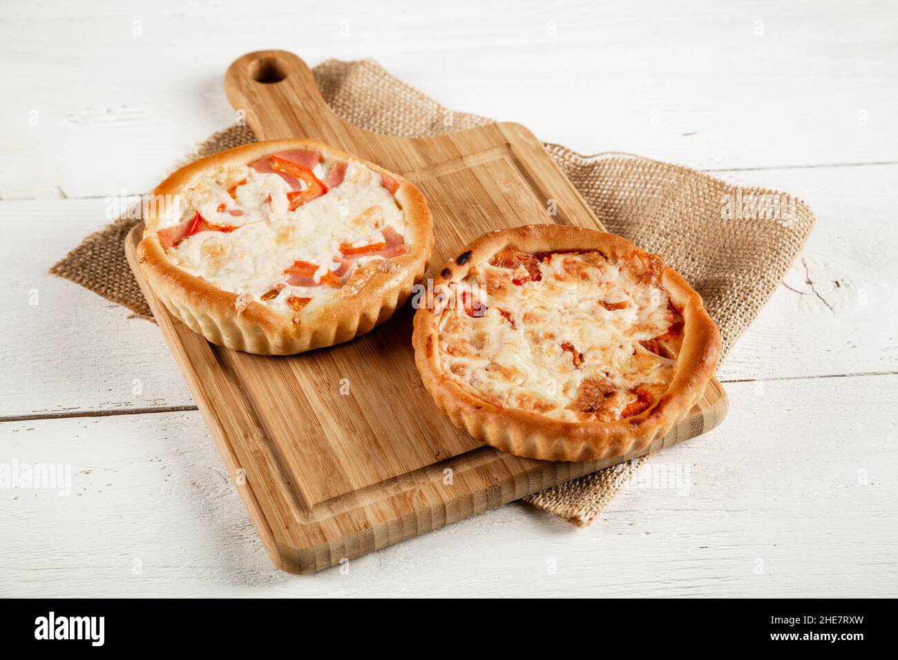 Due deliziose pizze su un tagliere su sfondo bianco in legno. Stile rustico. Foto Stock
