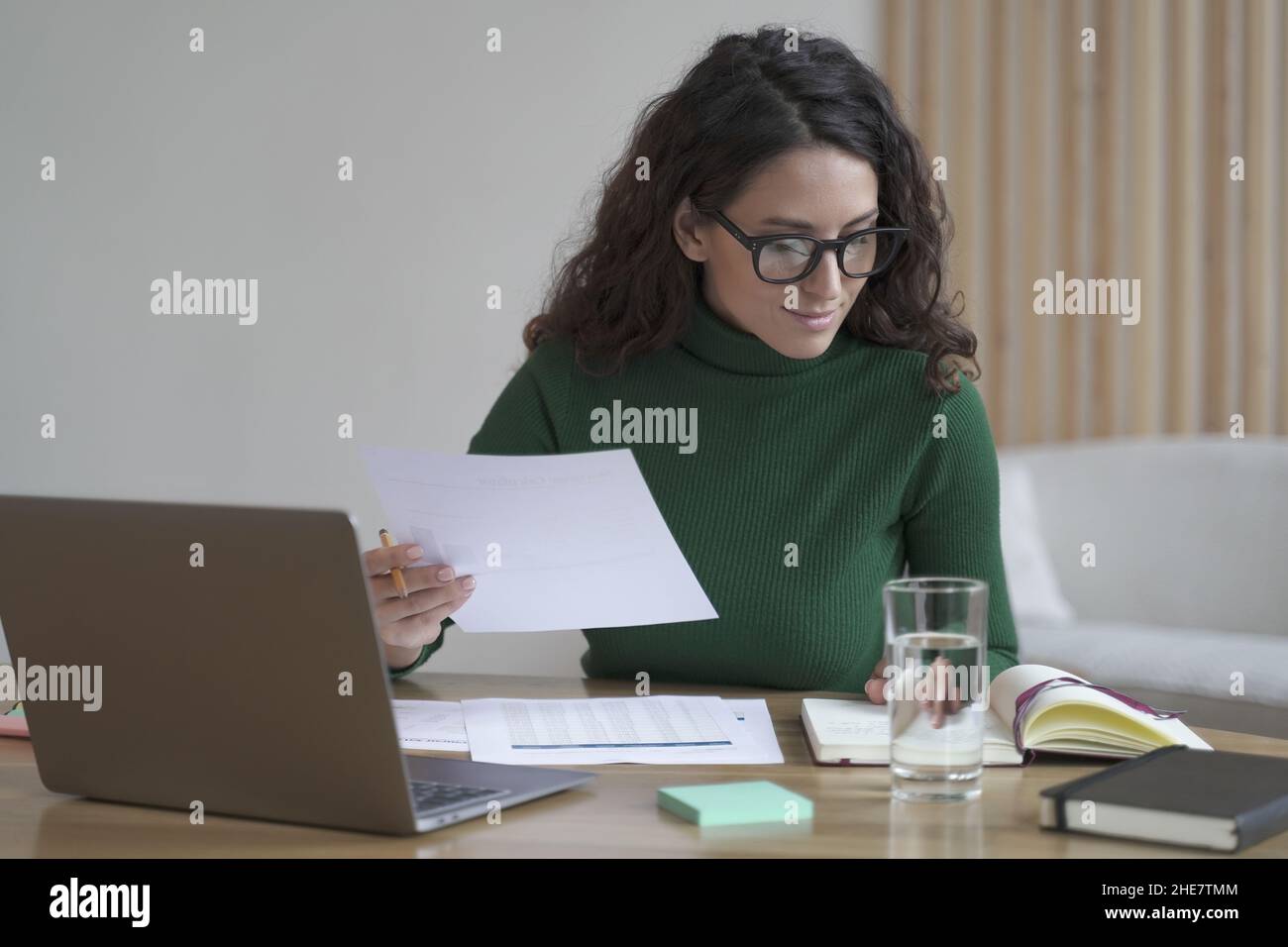 Giovane simpatica femmina italiana in occhiali preparazione report mentre si lavora su laptop in ufficio moderno Foto Stock