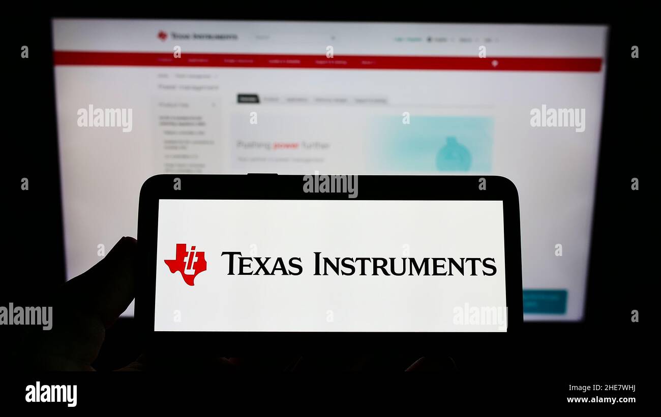 Persona che tiene il cellulare con il logo della società americana Texas Instruments Incorporated (ti) sullo schermo di fronte alla pagina web. Mettere a fuoco sul display del telefono. Foto Stock