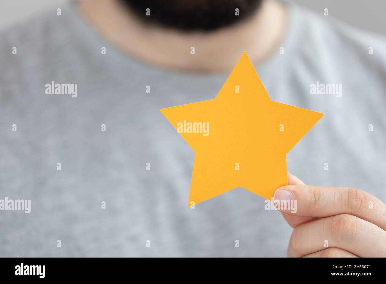 Maschio sfocato che tiene una stella gialla della carta, i concetti di feedback, di revisione e di valutazione Foto Stock