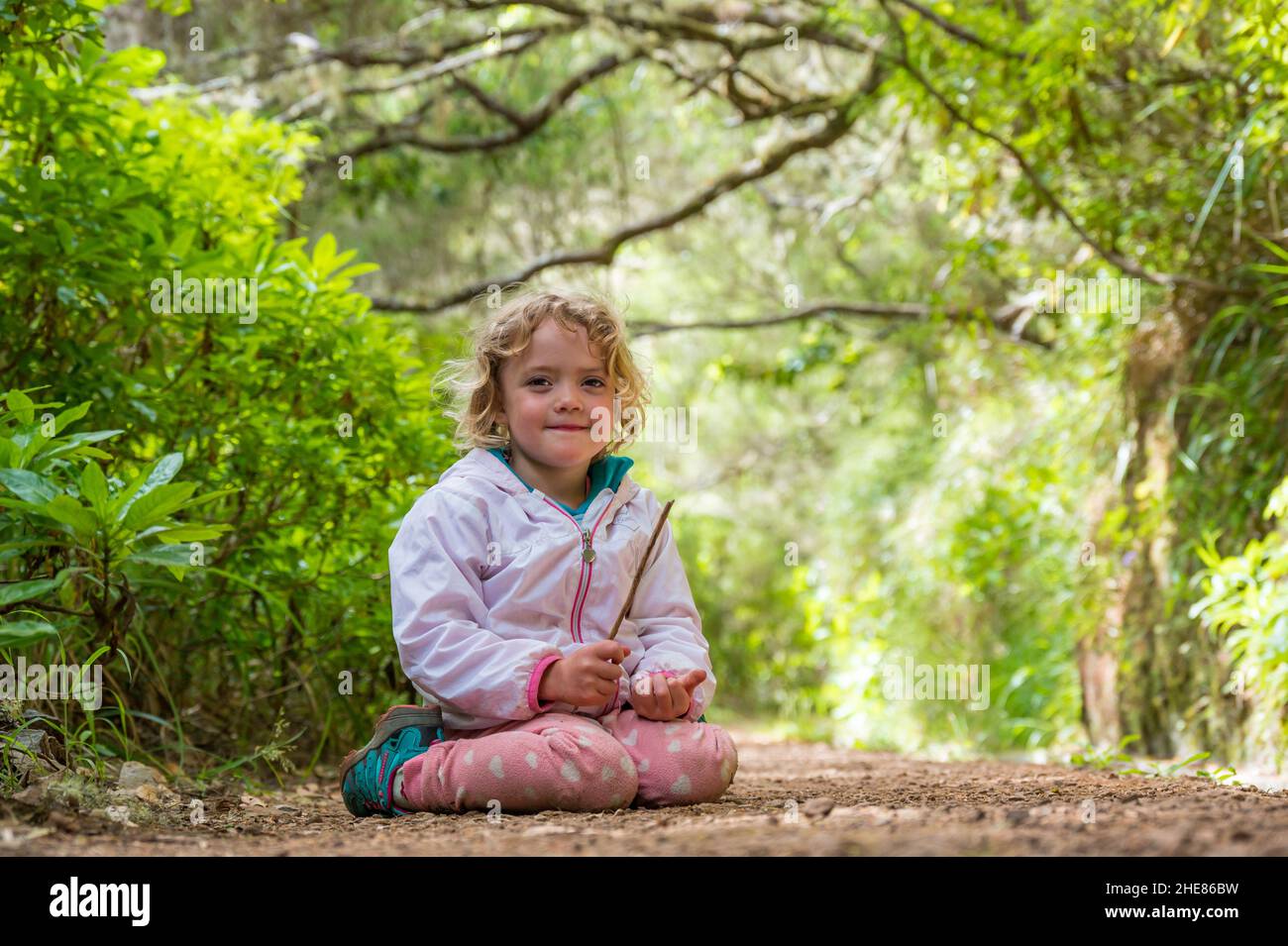 Simpatica ragazza bionda seduta sul sentiero forestale godendo la natura e posa. Foto Stock