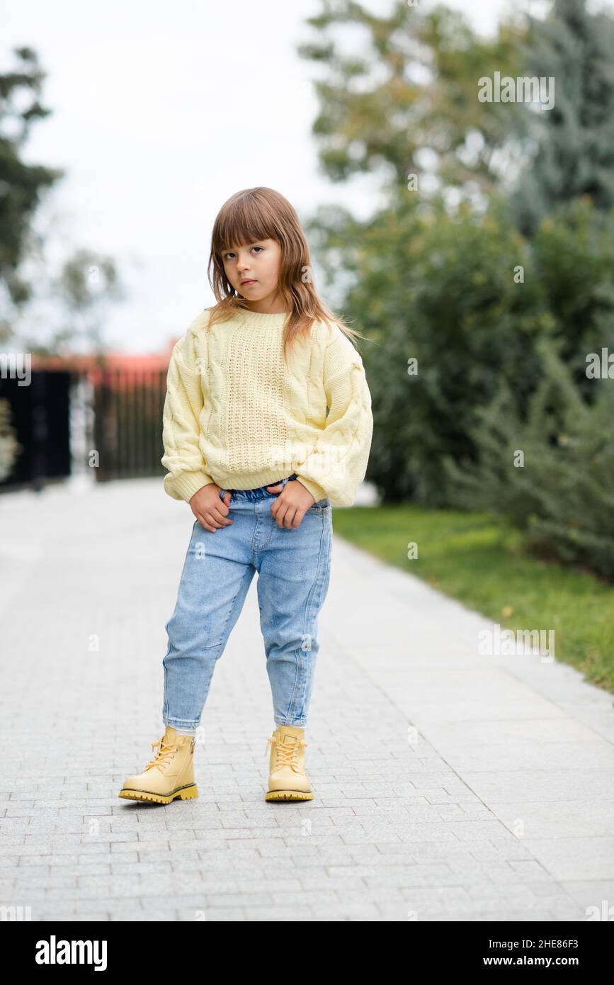 La ragazza di capretto di 5-6 anni di stile indossa il pullover casual alla moda e pantaloni jeans che camminano nel parco all'aperto. Primavera. Bambino piccolo sopra la natura primavera backgro Foto Stock