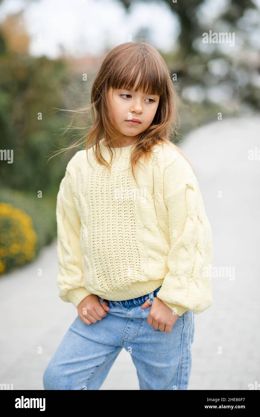 La ragazza di capretto di 5-6 anni di stile indossa il pullover casual alla moda e pantaloni jeans che camminano nel parco all'aperto. Primavera. Bambino piccolo sopra la natura primavera backgro Foto Stock