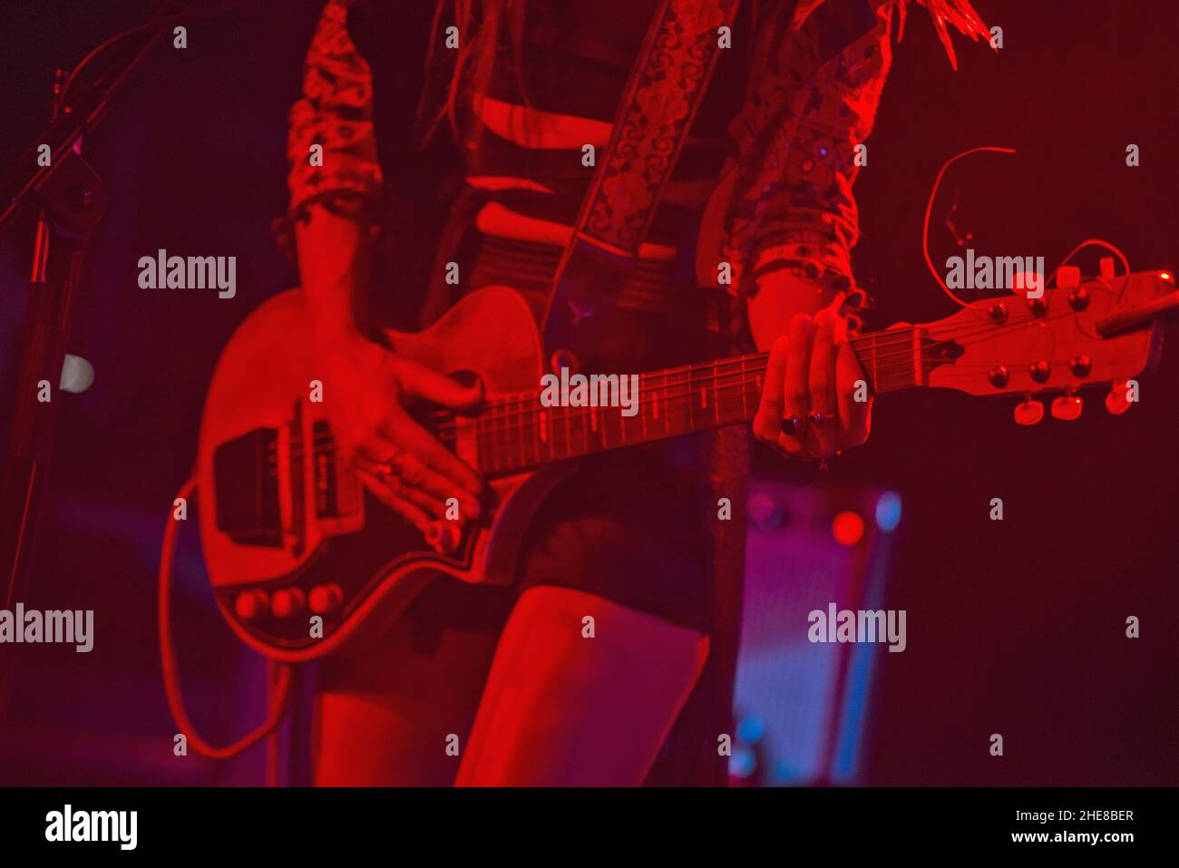 Primo piano di una donna che suona chitarra elettrica sul palco durante un concerto con luci rosse Foto Stock